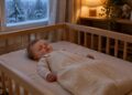 Baby sleeping safely on their back in a sleep sack in a winter nursery, with a room thermometer on the shelf